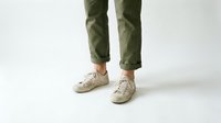 Casual male legs in olive green pants and beige sneakers standing on white background. Modern menswear fashion style for everyday comfort and urban lifestyle.