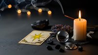 Mystical fortune telling setup with tarot cards, crystal ball, burning candle and occult symbols on dark surface with atmospheric lighting for divination.
