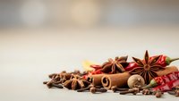 Aromatic spices including cinnamon sticks, star anise, cloves and chili peppers arranged on neutral background for culinary and cooking projects.