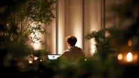 Man working late at night on laptop in modern office with warm ambient lighting and plants creating cozy productive workspace atmosphere for remote work.