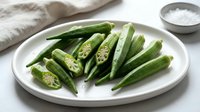 Fresh green okra pods sliced and whole on white plate, healthy organic vegetable ingredient for cooking and nutrition recipes.