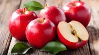 Fresh red apples with water drops and green leaves on rustic wooden background, one cut in half showing white flesh and seeds. For food and harvest concepts.