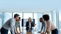 Young diverse business team collaborating in modern office with city skyline view, discussing strategy and ideas during meeting.