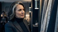 Mature businesswoman with gray hair in elegant suit examining fabric samples in upscale showroom for interior design consultation and textile selection.