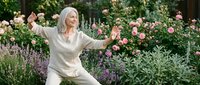 Senior Caucasian woman practicing tai chi in blooming garden with pink roses and lavender, peaceful outdoor exercise for wellness and mindfulness.