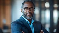 Professional African American businessman with glasses and beard in modern office environment for corporate marketing materials.