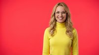 Happy blonde woman in yellow turtleneck sweater smiling at camera against bright red background for lifestyle and fashion content.