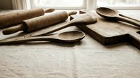 Wooden kitchen utensils and rolling pins arranged on linen fabric near window creating rustic cooking and baking scene for culinary designs.