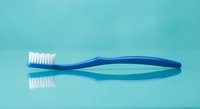 Blue toothbrush with white bristles on turquoise background for dental hygiene and oral care concepts.