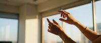 Female hands holding smartphone with warm sunlight streaming through modern office window creating natural lighting for mobile technology and communication.