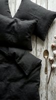 Dark charcoal linen bedding set with pillows on rustic white wooden background, natural textile home decor for bedroom interior design and styling.