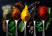 Vibrant aromatic spices and herbs arranged in silver spoons on dark background, including turmeric, paprika, black peppercorns, bay leaf and fresh herbs for cooking.