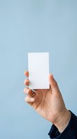 Hand holding blank white card against soft blue background, ideal for business card mockups, greeting card designs, and promotional material presentations.