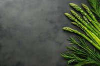 Fresh green asparagus spears and dill arranged on dark stone background with copy space, top view composition for food photography and menu design.