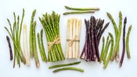 Fresh asparagus spears in green, white and purple varieties arranged on white background, isolated for culinary design and healthy cooking concepts.