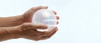 Hands protecting transparent glass sphere with glowing light inside symbolizing care, protection, environmental conservation and sustainable future concepts.