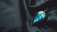 Close-up of labradorite gemstone pendant with blue-green iridescent flash on dark fabric background showcasing natural mineral beauty and mystical properties.