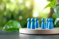 Blue wooden figures arranged in groups on circular wooden base against blurred green natural background, representing teamwork and community.