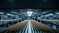 Modern industrial brewery facility with rows of glass bottles on conveyor system under bright LED lighting for beverage production and manufacturing operations.