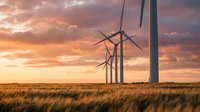 Wind turbines generating renewable energy in golden wheat field at sunset with dramatic orange sky and clouds creating sustainable power landscape.