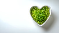 Fresh microgreens in heart-shaped white ceramic bowl on minimalist background, symbolizing healthy eating and love for nutritious food.