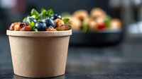 Fresh blueberries and roasted nuts in eco-friendly kraft paper bowl on dark background with copy space. Healthy organic snack concept for food service.