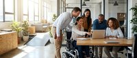Diverse business team collaborating in modern office with wheelchair accessibility, promoting inclusive workplace culture and teamwork.