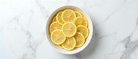 Fresh lemon slices arranged in a white bowl on a marble surface, top view. Bright citrus fruit for healthy food and cooking concepts.