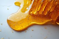 Fresh golden honey dripping and flowing with tiny air bubbles on white surface, macro close up view showing natural sweetener texture and viscosity.