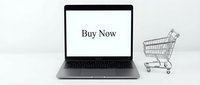 Laptop with Buy Now text on screen next to a miniature shopping cart on white background, symbolizing e-commerce and online shopping.