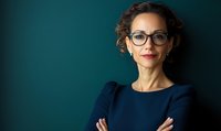 Professional businesswoman with glasses and curly hair wearing navy blue dress standing confidently with arms crossed against dark green background.