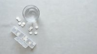 White pills and tablets scattered near glass of water on light surface for medication and healthcare concepts.