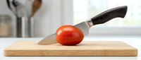 Fresh ripe tomato being sliced with sharp kitchen knife on wooden cutting board in bright modern kitchen, food preparation and cooking concept.