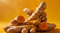 Fresh ginger root with turmeric powder on warm golden background. Natural spice ingredients for cooking, health supplements and wellness products.