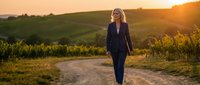 Professional businesswoman walking on rural path through vineyard at golden hour sunset, representing success, leadership and work-life balance journey.