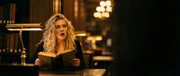 Young blonde woman reading book in elegant library with warm lighting and vintage atmosphere for education and literature concepts.