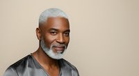 Mature African American man with gray hair and beard wearing black shirt against neutral background, studio portrait.