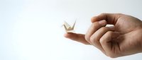 Male hand holding delicate white paper crane origami on white background, symbolizing peace, hope, and Japanese tradition for design projects.