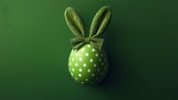 Green Easter egg decorated with white polka dots and fabric bunny ears bow on dark background, festive holiday concept for seasonal designs.