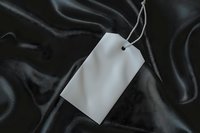 Blank white price tag or label with string on luxurious black silk fabric background, creating elegant contrast for retail and fashion marketing.