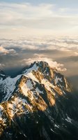 Majestic snow-capped mountain peak bathed in golden sunrise light with dramatic clouds and misty valleys below for outdoor adventure and nature content.