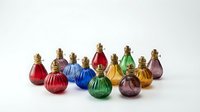 Colorful glass perfume bottles with gold caps arranged on white surface, featuring red, blue, green, yellow and purple hues for fragrance, cosmetics and luxury product displays.