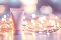 Pink cosmetic tube on reflective surface with warm fairy lights creating romantic bokeh background. Minimal beauty product photography for skincare advertising.