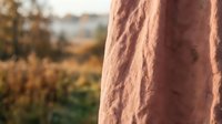 Rustic terracotta fabric hanging outdoors with blurred autumn landscape background, suitable for textile, fashion, and lifestyle design projects.