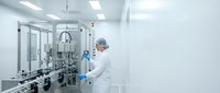 Pharmaceutical technician in sterile cleanroom operating automated filling equipment for drug manufacturing and quality control processes.