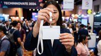 Young woman of East Asian descent displaying blank event badge at technology conference with crowded venue background, suitable for corporate, business, and conference marketing materials.