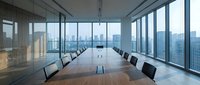 Modern corporate boardroom with long wooden conference table and black chairs overlooking city skyline through floor-to-ceiling windows for business meetings.