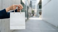 Woman in dark business attire holding blank white shopping bag on urban street, suitable for retail, commerce, and lifestyle marketing campaigns.