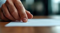Close up view of male hand touching blank white paper on wooden desk surface in soft natural lighting, creating minimalist composition for business concept.