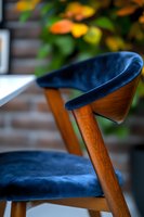 Mid-century modern dining chair with navy blue velvet upholstery and walnut wood frame, close-up detail view against blurred autumn background.